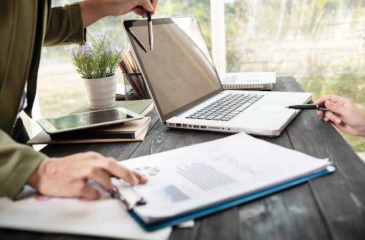 A business professional reviewing financial charts and documents next to an open laptop